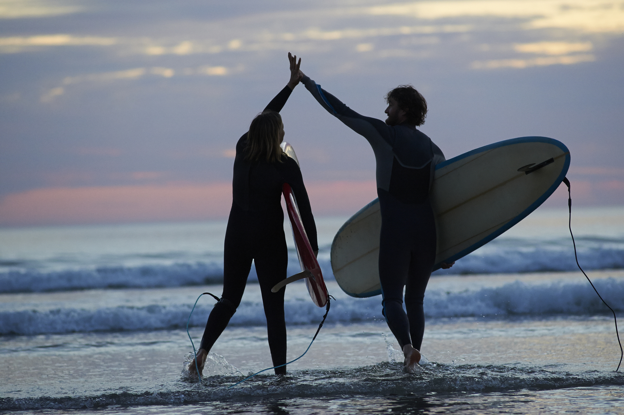 Surfers high-fiving at sunset